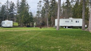 Un camping con dos vehículos recreativos, un campo césped y árboles.