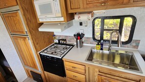 Cocina compacta de autocaravana con estufa, pileta, alacenas de madera y ventana.