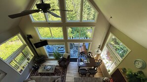 A spacious living area with a high ceiling, large windows, and a ceiling fan. - Peaceful, private 1-bedroom + loft bedroom home nestled in the forest. (Saltspring Island)