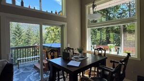 A spacious dining area with a high ceiling and large windows offering views of a lush garden. - Peaceful, private 1-bedroom + loft bedroom home nestled in the forest. (Saltspring Island)