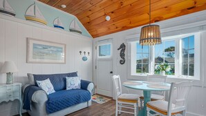 A cozy room with a wooden ceiling, a blue sofa with starfish pillows, a white door, and a round table with white chairs. - Catch a Cape Escape at By The Sea (South Yarmouth)