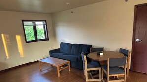A room with a wooden floor, a blue sofa, a small wooden table, and a round wooden table with chairs. - Apartment Centrally Located (Plymouth)