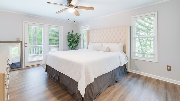 A bedroom with a large bed, a ceiling fan, and a view of the outdoors through the windows.