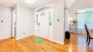 A hallway with hardwood floors, a white door with glass panels, a small rug, and a potted plant by a window.