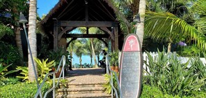 A wooden structure with a thatched roof, surrounded by lush greenery and palm trees.