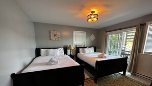 Een hotelkamer met twee bedden, een groot raam met luxaflex, een decoratief vloerkleed en een plafondlamp.