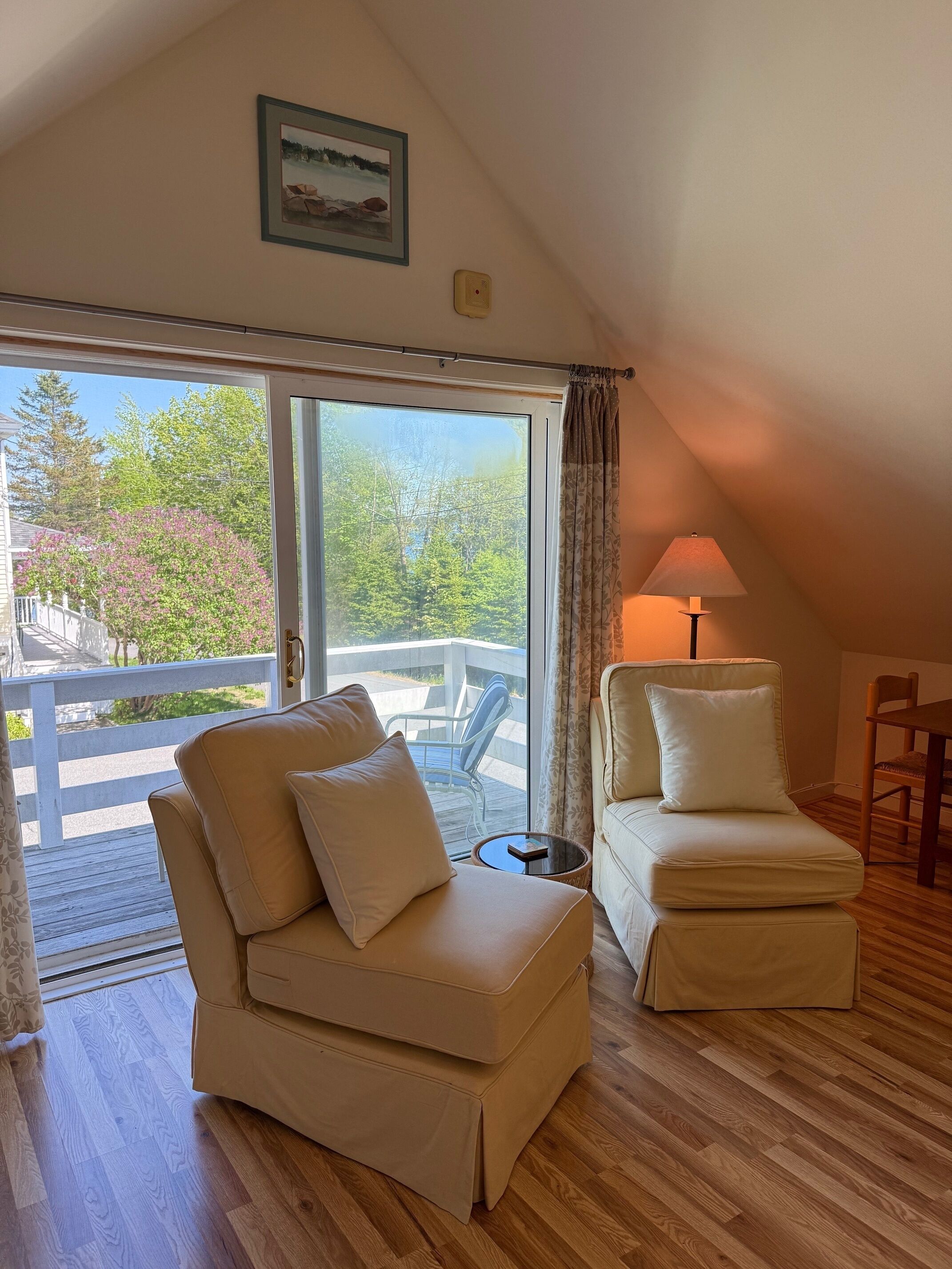 A cozy room with a large window, a ceiling lamp, and a framed picture on the wall.