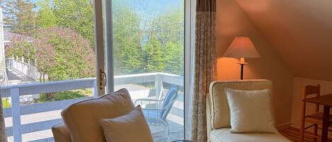 A cozy room with a large window, a ceiling lamp, and a framed picture on the wall.