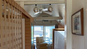 Ein Flur mit Holzboden, Deckenventilator und Blick auf einen Balkon mit Stuhl und Tisch.