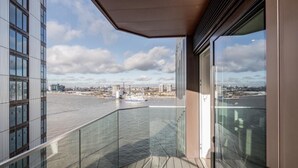 Un balcón con vista a un río y un paisaje urbano, con edificios modernos y un barco.