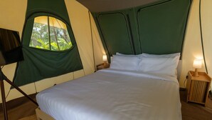 A bed with a green headboard and a window, a lamp on the side, and a wooden floor.