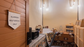 A small, cozy room with a wooden wall, a table with a patterned tablecloth, a TV, and a sign indicating self-service for lockers.