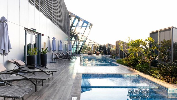 An outdoor swimming pool area with lounge chairs and a glass-enclosed seating area. - Premium Corner Apt 1BD in JONE w Canal View (Dubai)