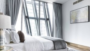 A modern bedroom with a large bed, a bedside table, a lamp, and a window with curtains. - Premium Corner Apt 1BD in JONE w Canal View (Dubai)