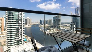 A balcony with a view of a city skyline, a body of water, and a wooden table. - Premium Corner Apt 1BD in JONE w Canal View (Dubai)