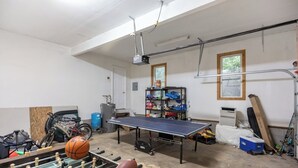 A garage with a ping pong table, a foosball table, and various sports equipment. - Spacious 4BR Getaway w/ Games, Pier & Firepit (King and Queen Court House)