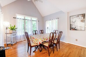 A dining room with a wooden table and chairs, large windows, and a ceiling fan. - Spacious 4BR Getaway w/ Games, Pier & Firepit (King and Queen Court House)