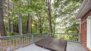A covered outdoor deck with a bench, surrounded by trees and a brick wall. - Spacious 4BR Getaway w/ Games, Pier & Firepit (King and Queen Court House)