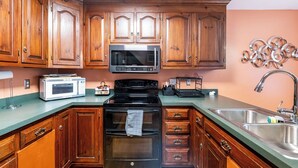 A kitchen with wooden cabinets, a microwave, a stove, and a sink. - Spacious 4BR Getaway w/ Games, Pier & Firepit (King and Queen Court House)