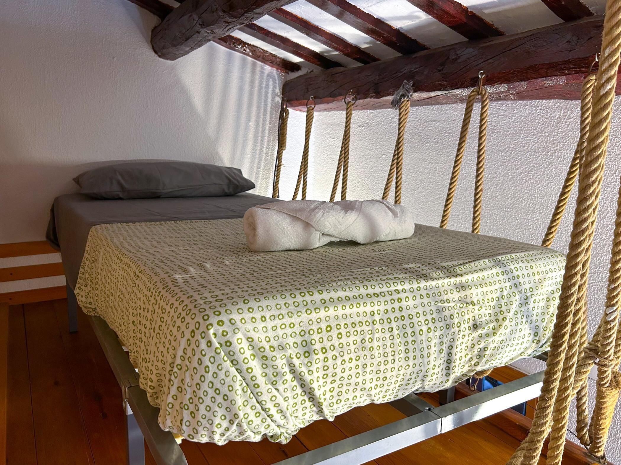 Ein Bett mit einem gemusterten Überwurf, einem grauen Kissen und einem gefalteten Handtuch.