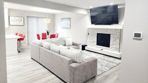 Una sala de estar moderna con un sofá gris, sillas rojas, una chimenea y un televisor de pantalla plana montado encima.
