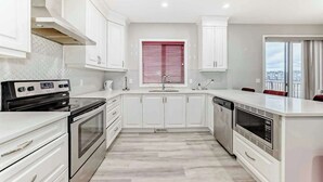 A modern kitchen with white cabinetry, a built-in oven, a dishwasher, and a window with red blinds.