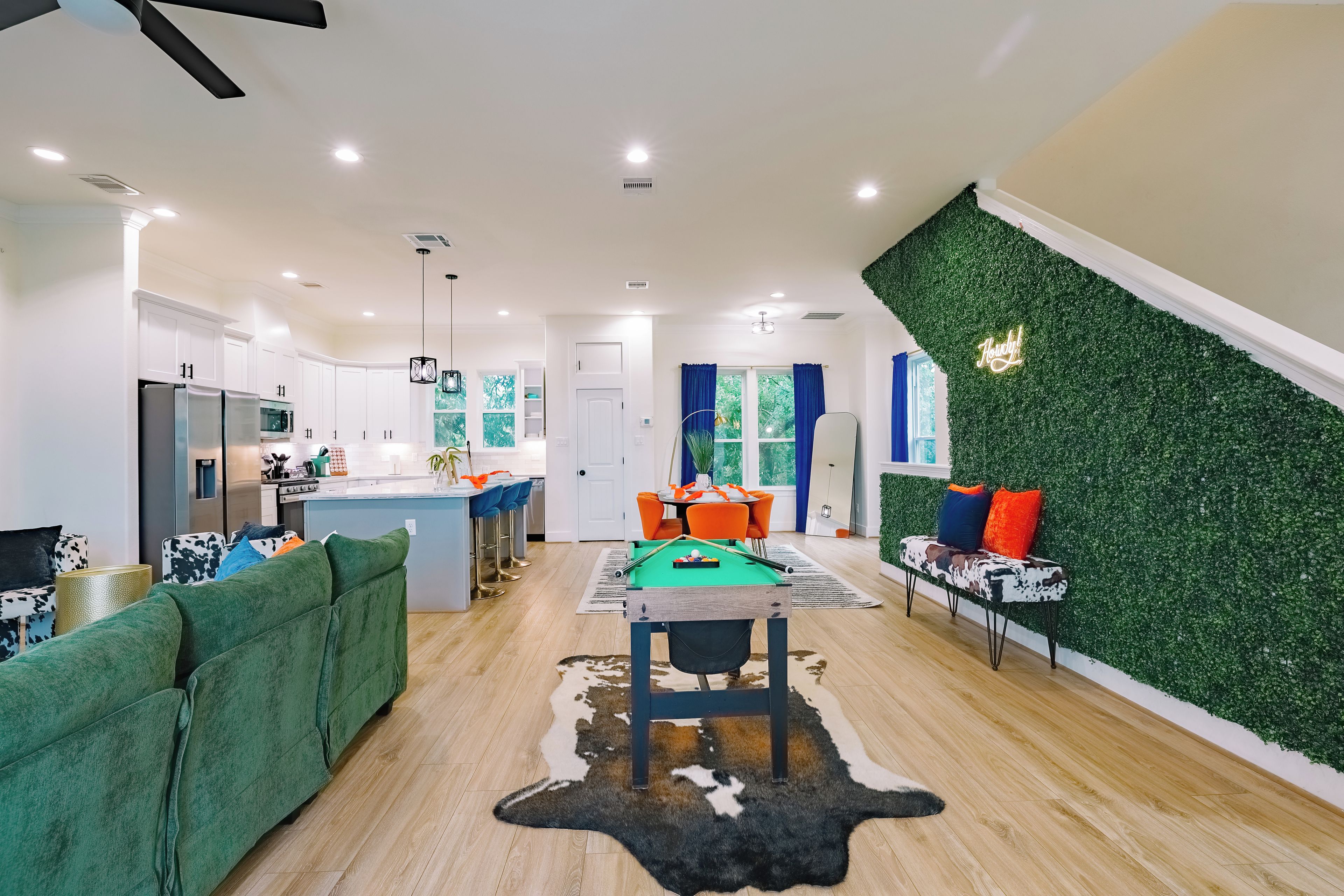 A modern kitchen with white cabinets, a dining area with a pool table, and a living room with a green sofa and a cowhide rug.