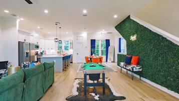 A modern kitchen with white cabinets, a dining area with a pool table, and a living room with a green sofa and a cowhide rug.