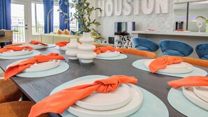 A dining table set with plates, napkins, and vases, with a view of a living area in the background. - Modern Retreat w/ Rooftop Cinema (Houston)