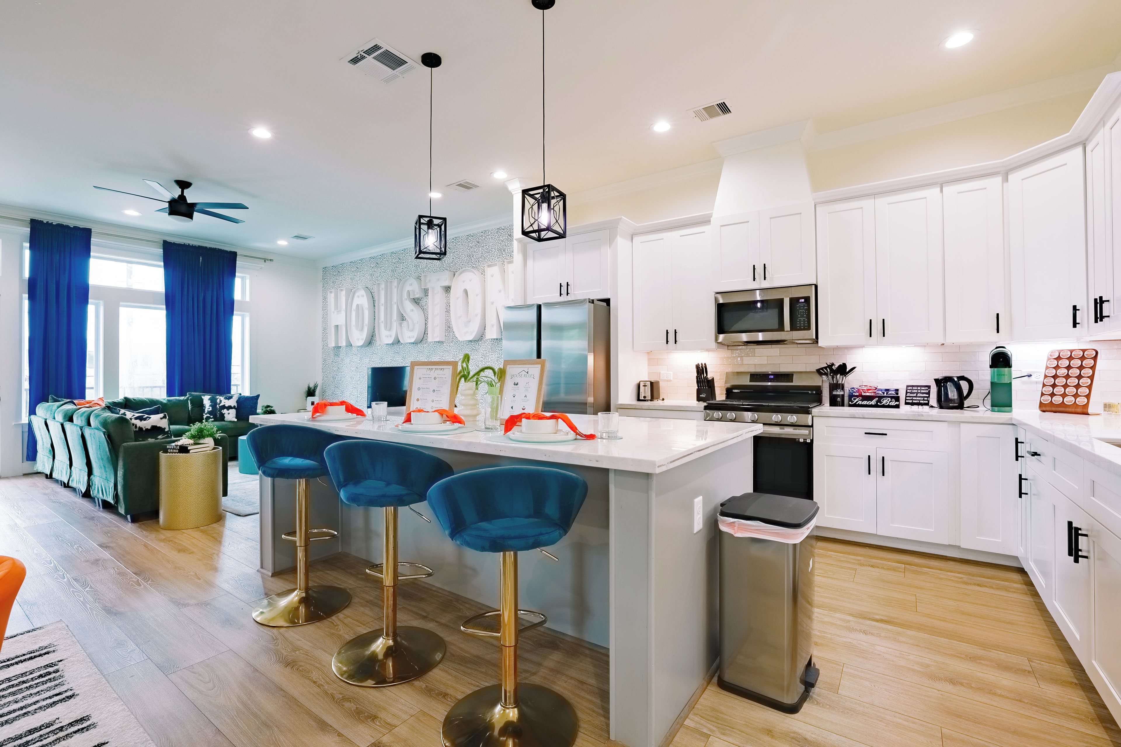 A modern kitchen with white cabinets, a central island with bar stools, and a dining area with a sofa and curtains.