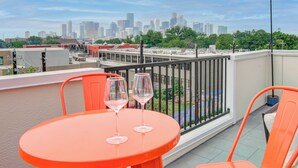 A rooftop terrace with a table and chairs, two wine glasses, and a city skyline view. - Modern Retreat w/ Rooftop Cinema (Houston)