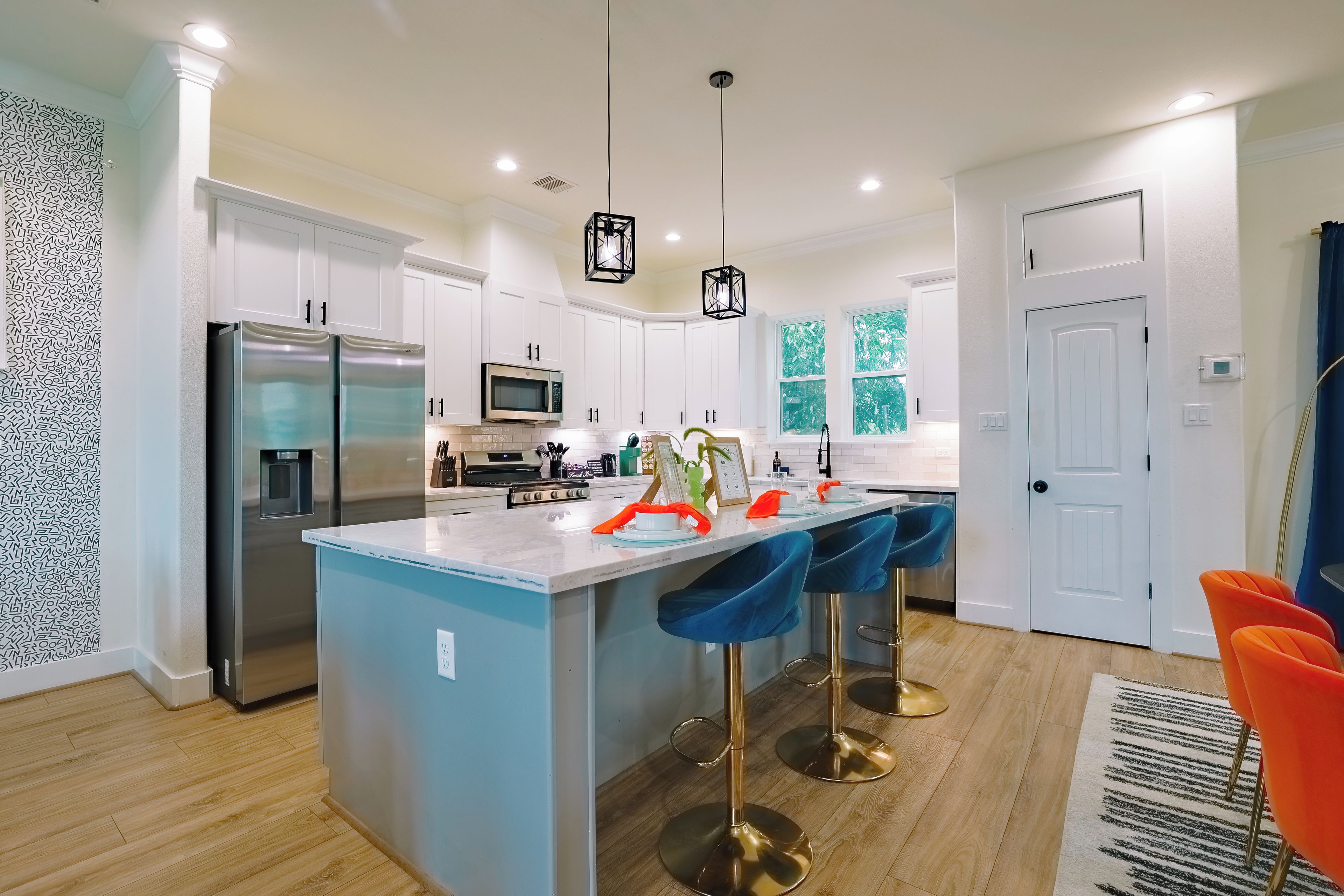 A modern kitchen with white cabinets, stainless steel appliances, a central island with bar stools, and a view of the outdoors through large windows.
