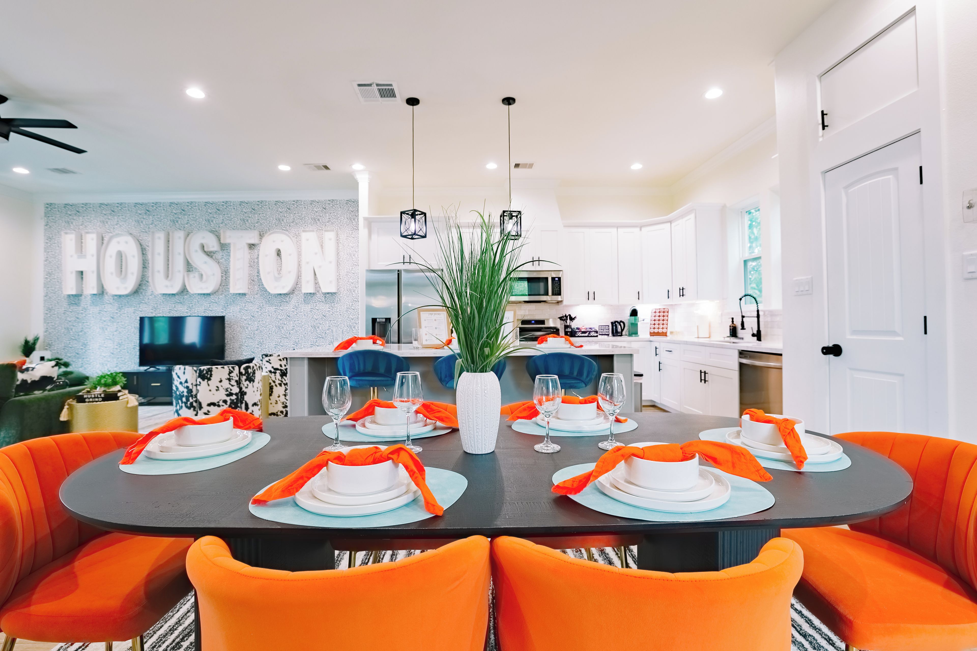 A modern dining area with a large table set for six, surrounded by orange chairs.