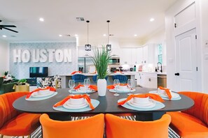 A modern dining area with a large table set for six, surrounded by orange chairs. - Modern Retreat w/ Rooftop Cinema (Houston)