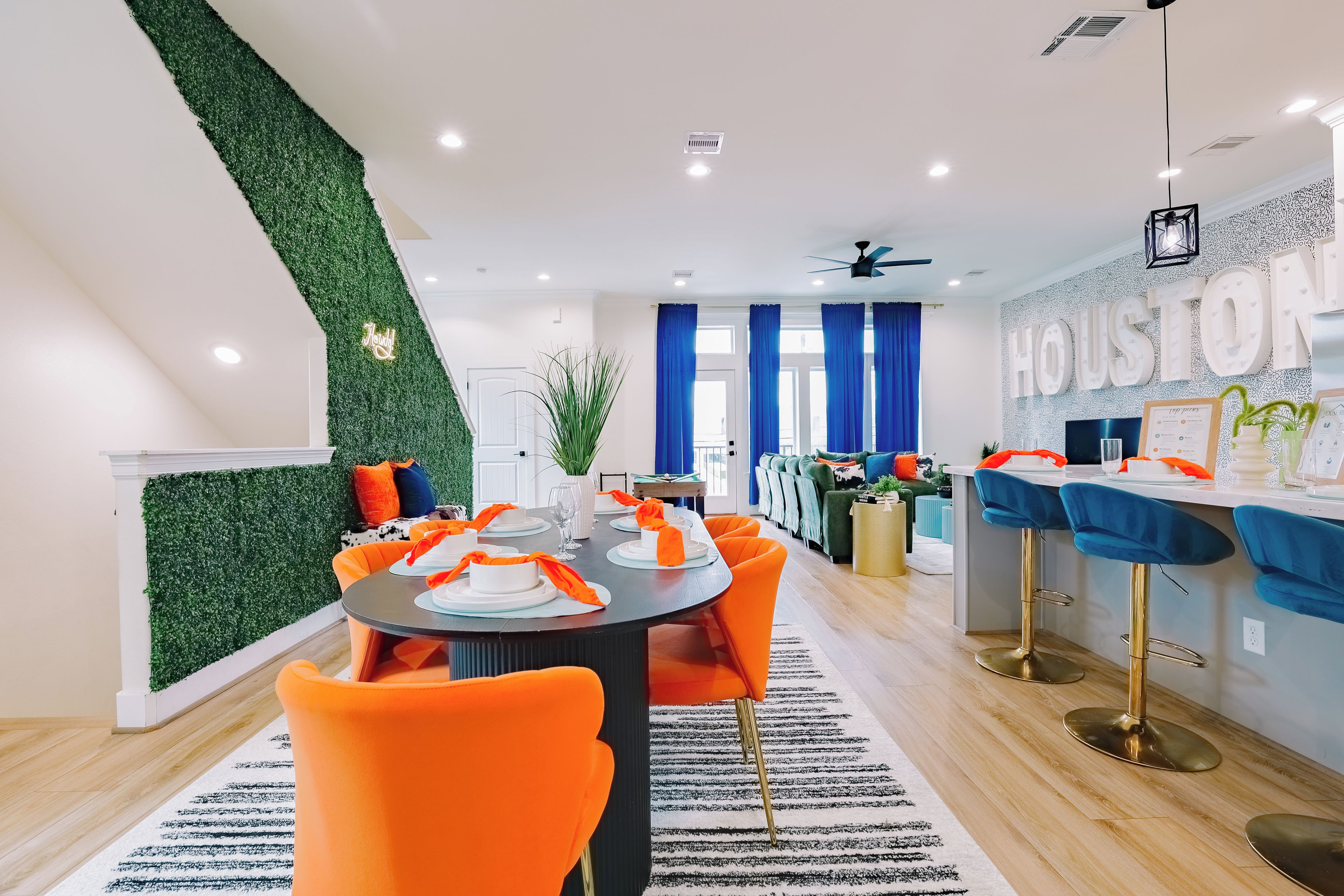 A modern kitchen with a bar area, a dining room with orange chairs, and a living area with a green wall.