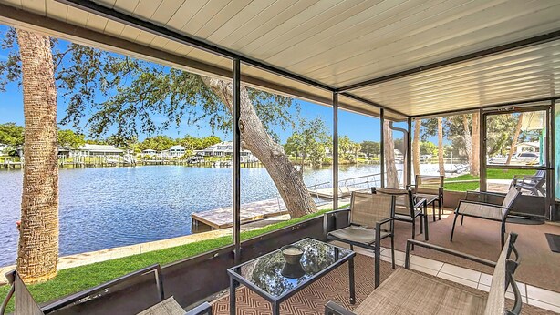 Un espace extérieur abrité avec des places assises, offrant une vue sur un lac, une terrasse en bois et des chaises.