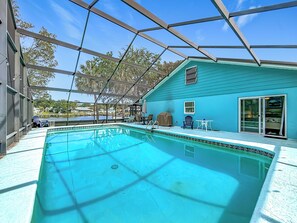 A swimming pool with a covered deck, a house with a blue exterior, and a view of the surrounding area. - New VRBO 2026 open dates-New 4/3 with heated pool, dock, kayaks, outdoor space (Crystal River)