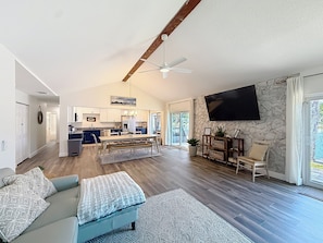 A spacious living area with a sofa, a dining table, and a kitchen in the background. - New VRBO 2026 open dates-New 4/3 with heated pool, dock, kayaks, outdoor space (Crystal River)