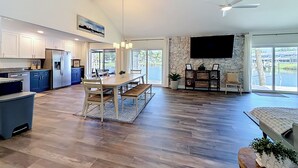 Une cuisine spacieuse équipée d’appareils modernes, un coin repas avec une grande table et un salon doté d’un téléviseur et d’un mur en pierre.