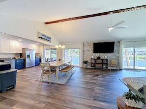 A spacious kitchen with modern appliances, a dining area with a large table, and a living room with a TV and stone wall. - New VRBO 2026 open dates-New 4/3 with heated pool, dock, kayaks, outdoor space (Crystal River)