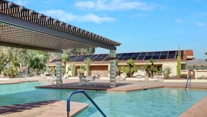 A pool area with a pergola, lounge chairs, and a building with solar panels.