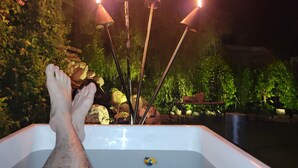 A bathtub with candles, surrounded by greenery and rocks.