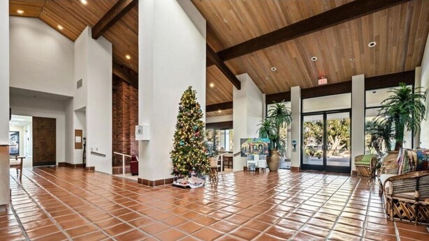 A spacious lobby with a tiled floor, a Christmas tree, and a seating area with wicker furniture.