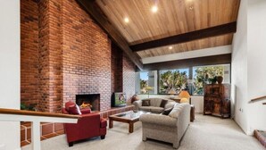A modern living room with a brick fireplace, comfortable seating, and large windows.