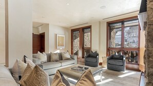 Een ruime woonkamer met een bank, fauteuils en een salontafel. Grote ramen bieden uitzicht op een besneeerd landschap.
