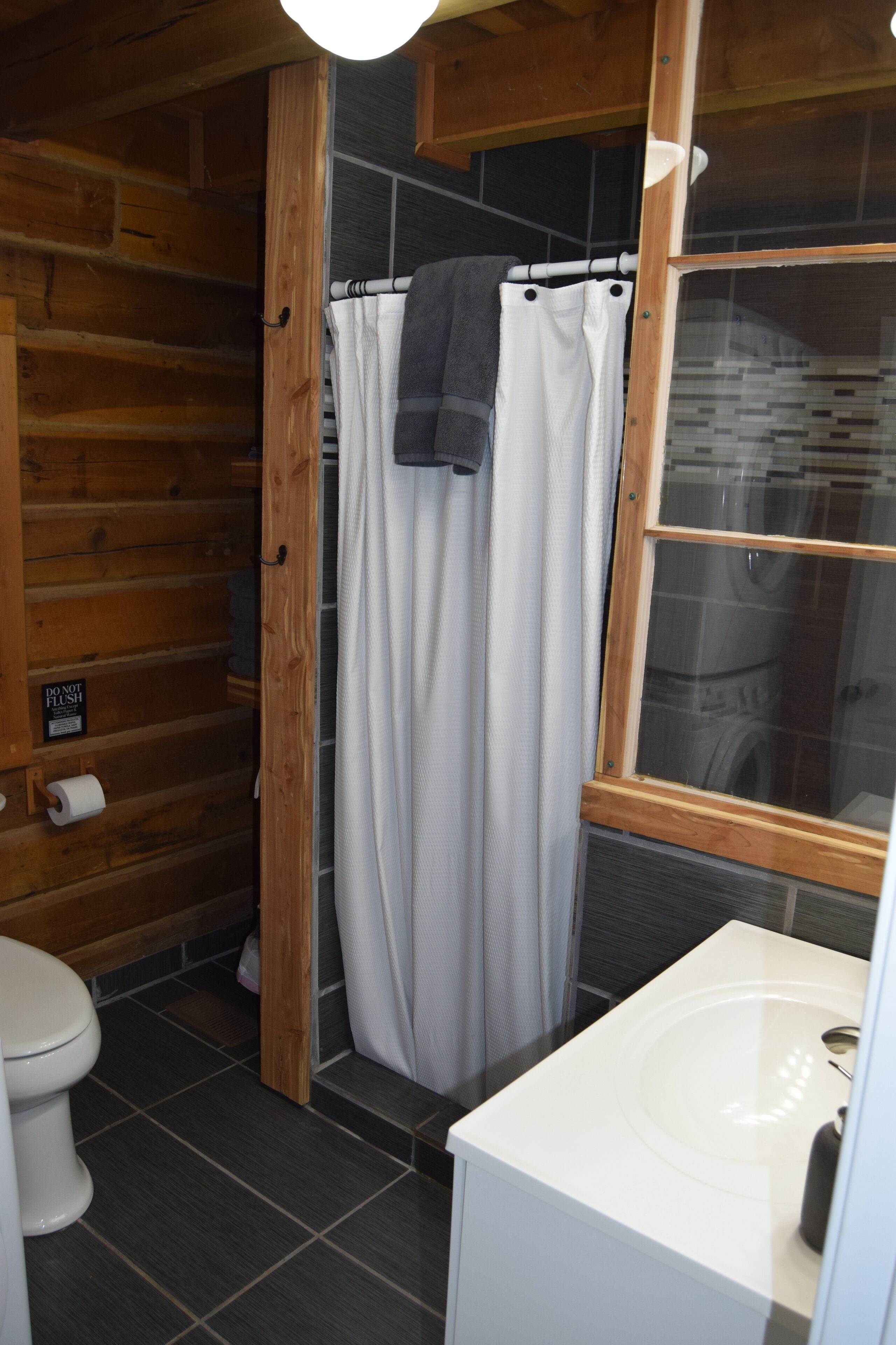 A bathroom with a wooden interior, a white sink, a shower curtain, and a toilet.