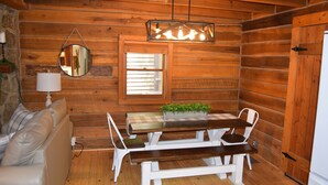 A wooden cabin interior with a white sofa, a wooden dining table with benches, a hanging mirror, and a window with blinds. - 3-bedroom cabin at Norris Lake, Sleeps 8 WiFi Lake access Covered boatslip (Speedwell)