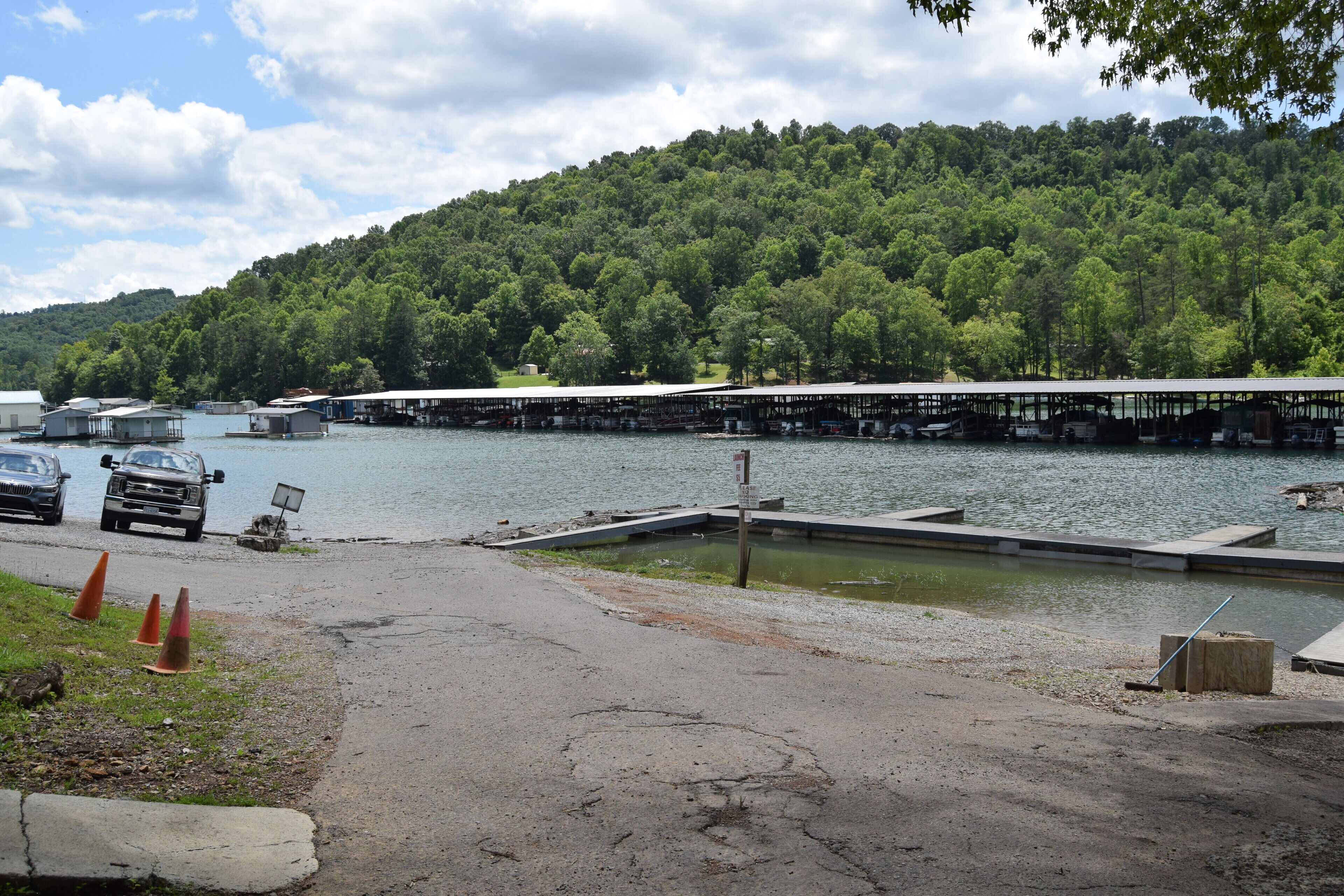 A lakeside dock with boats, a parking area, and a forested hillside.