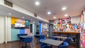 A modern interior with blue chairs and tables, a TV mounted on the wall, and colorful wall art. - Bunk Bed Room (4 Single Beds) (New York)