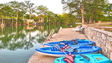 Un paisaje tranquilo junto al lago, con kayaks amarrados a un muelle de piedra, rodeado de exuberante vegetación y árboles.